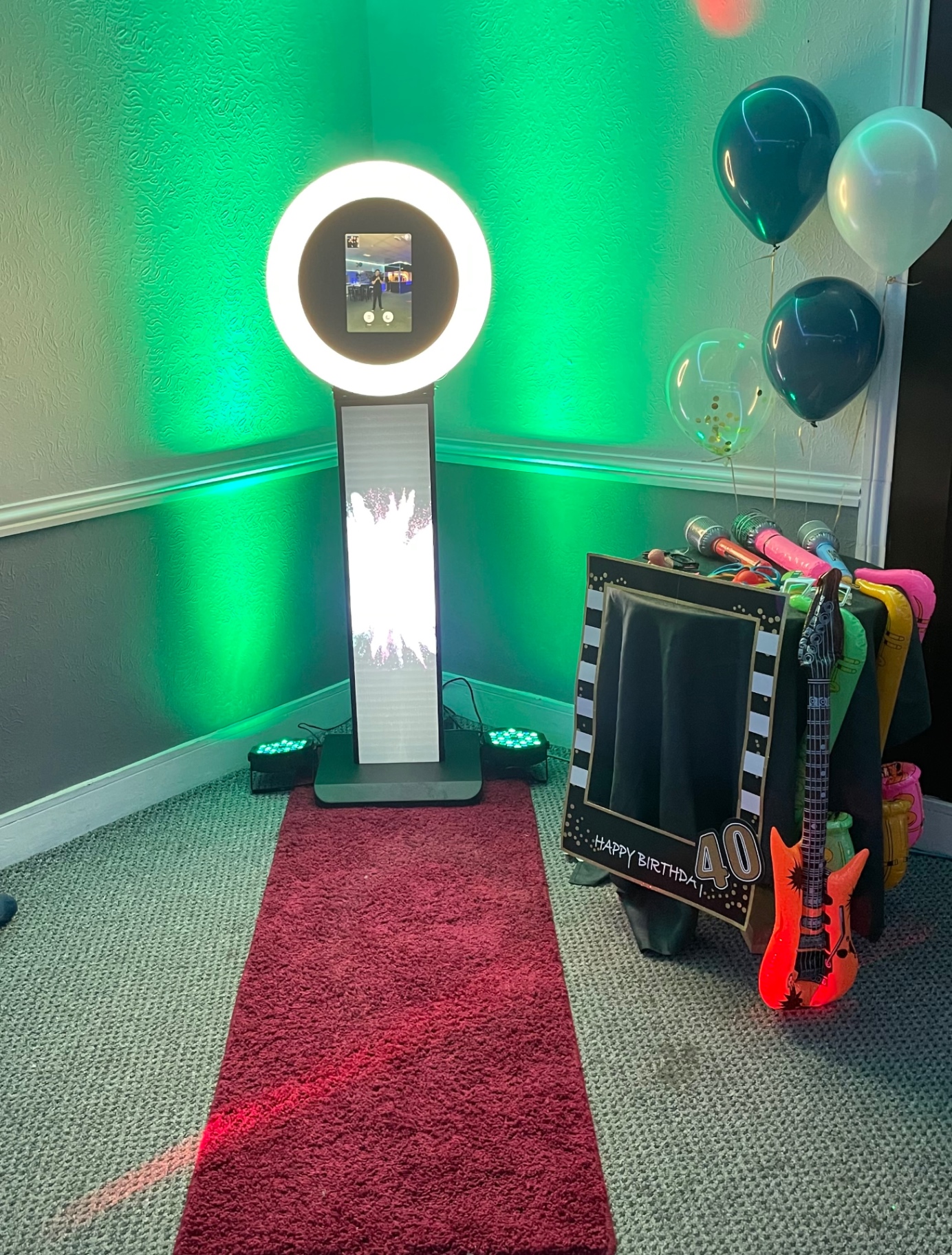 Selfie pod photo podium set up at a 40th birthday event with ring light, props, and red carpet.