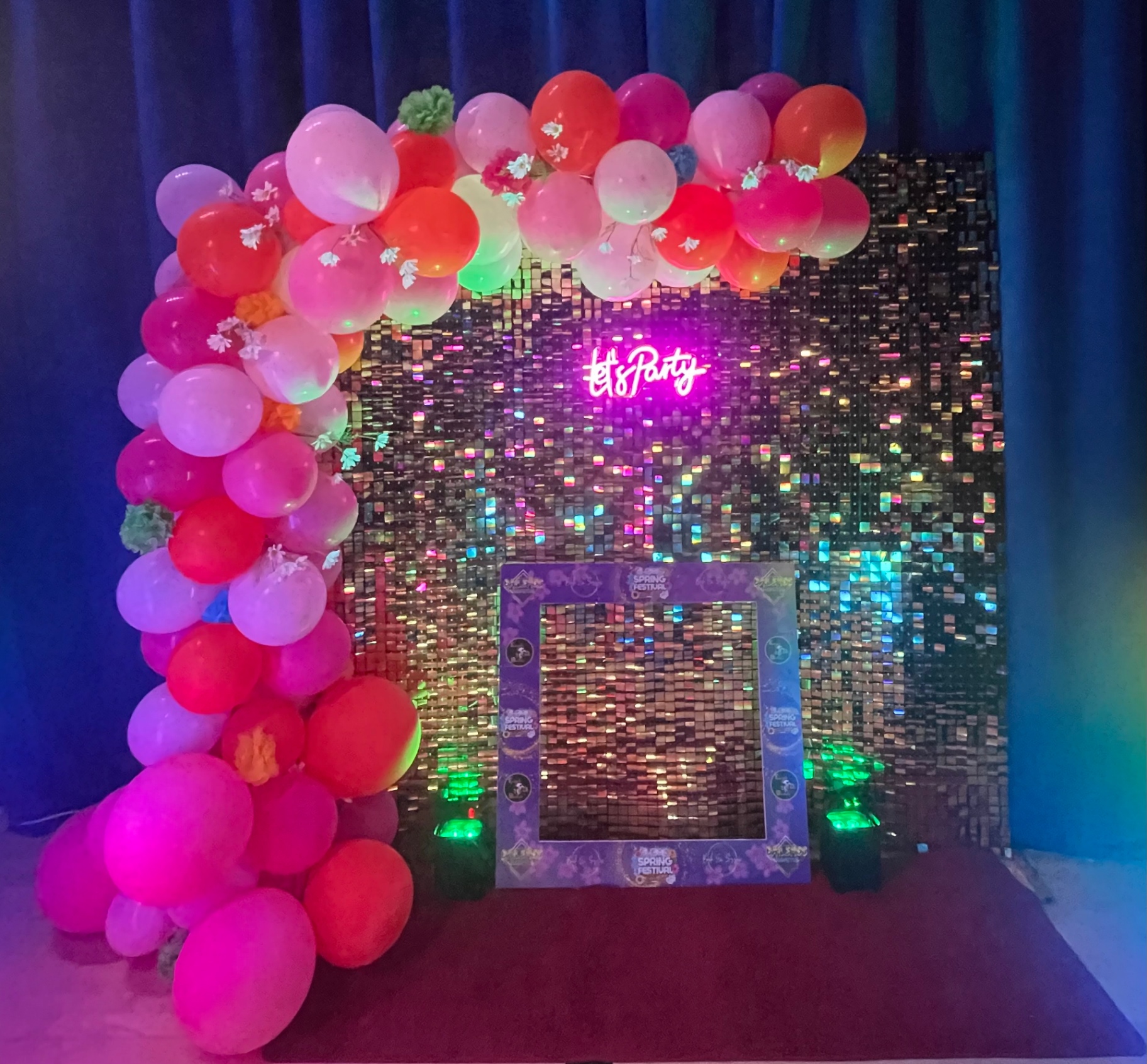 Shimmer wall backdrop with neon Let's Party sign and pink balloon arch at an event.