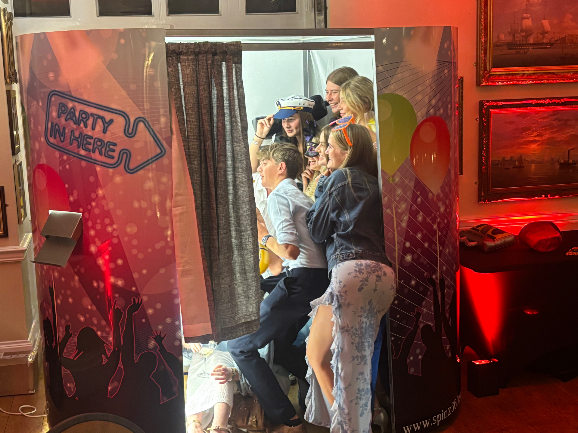 Guests posing together inside a traditional oval photobooth at an event.